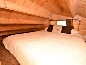 A bedroom with a wooden ceiling, a bed with white bedding, and two pillows with a design.