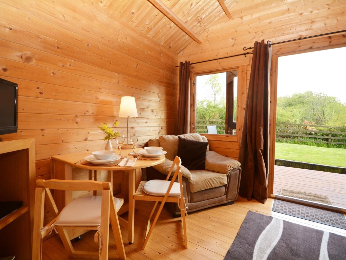 A wooden interior with a dining table set for two, a sofa, and a television.