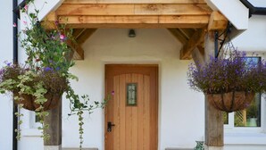 A wooden door with a glass panel, flanked by two hanging flower baskets on stone pedestals. - 3 Bed in Kingsbridge (oc-court) (South Huish)