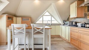 Une cuisine avec un plafond en bois, un coin repas avec des chaises blanches et une vue par la fenêtre.