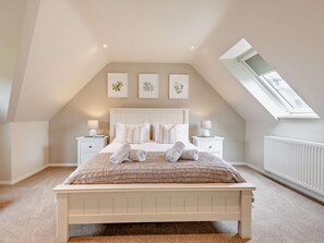 Ein Schlafzimmer mit schrägen Wänden, einem Dachfenster, einem Bett mit weißer Bettwäsche, zwei Nachttischen und drei an der Wand befestigten Bildern.