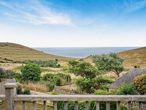 Eine Küstenlandschaft mit sanften Hügeln, wolkenlosem Himmel und Blick auf das Meer.