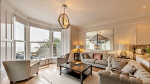 En rummelig stue med et stort vindue, en sofa, et sofabord og en iøjnefaldende geometrisk lampe.