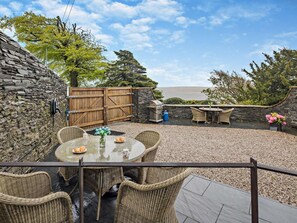 Eine Terrasse mit Korbmöbeln, einer Steinmauer und Blick auf das Meer.