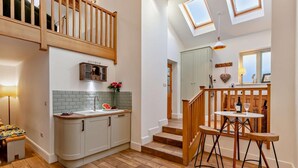 A modern kitchen with a wooden staircase, a dining area with stools, and a view of the sky through skylights. - 2 Bed in Settle (oc-g0051) (Settle)