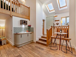 Eine moderne Küche mit einer Holztreppe, einem Essbereich mit Hockern und Blick zum Himmel durch Dachfenster.