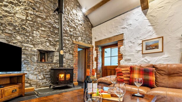 A cozy room with a stone wall, a fireplace, a leather sofa, and a wooden table with wine glasses. - 3 Bed in St Florence (oc-fb176) (Saint Florence)
