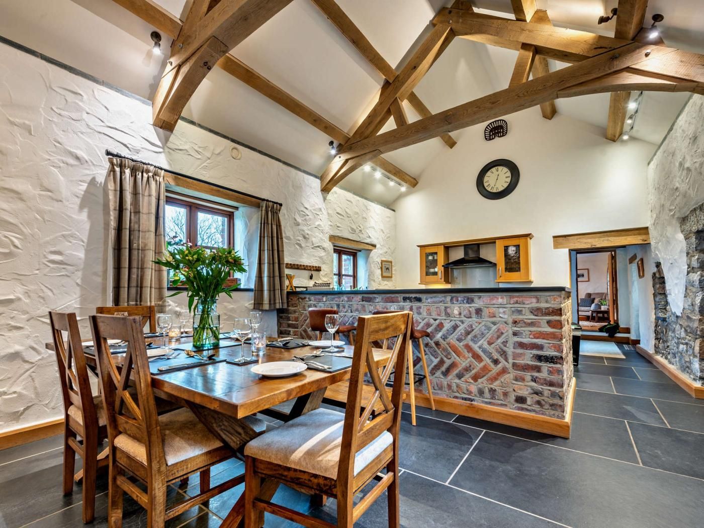 A rustic dining area with a wooden table and chairs, a brick wall, and a stone fireplace.