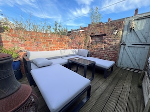A patio with a brick wall, a wooden deck, a white sofa, and a metal gate. - Heaton 1BDR Garden Flat With Dedicated Office (Tyne and Wear)