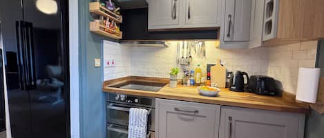 A modern kitchen with grey cabinets, a wooden countertop, a built-in oven, and a stainless steel refrigerator.