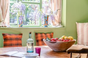 A dining table with a bowl of fruit, a bottle, and a book. - 2 Bed in Cirencester (oc-hic05) (Eastleach)