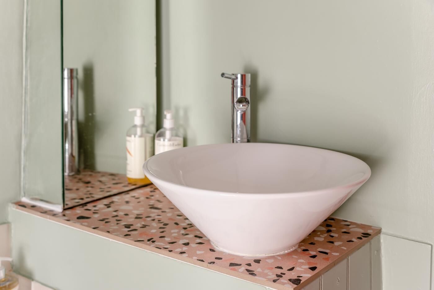 Une salle de bain avec un lavabo blanc, un miroir et un plan de toilette au motif terrazzo.