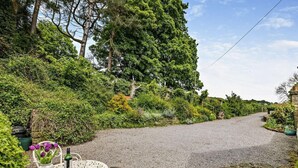 A gravel driveway leading to a house with a white metal table and chairs, surrounded by lush greenery and trees. - 1 Bed in Sheffield (oc-pk417) (Sheffield)