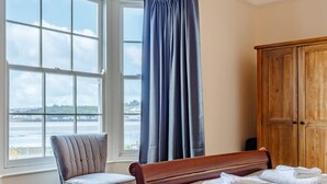 Ein Schlafzimmer mit einem Bett, einem Sessel, einem Kleiderschrank und einem Fenster mit Flussblick.