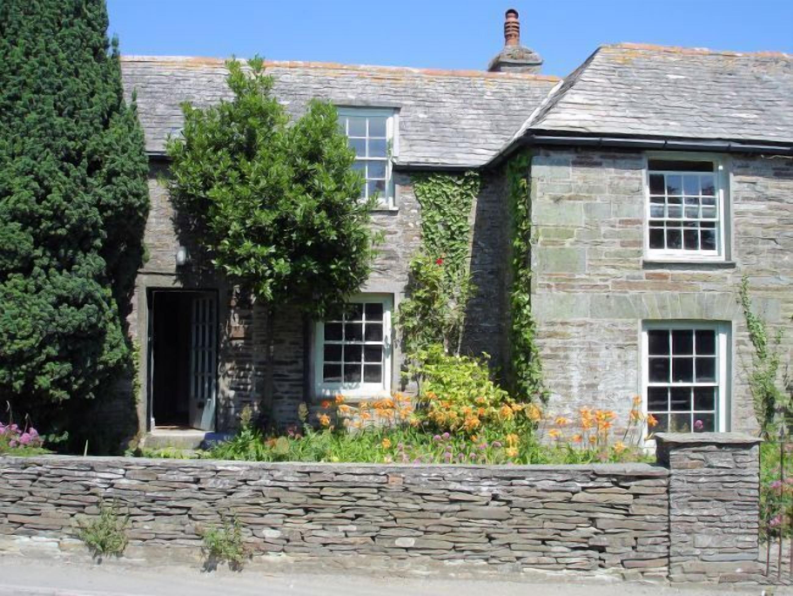 A stone house with a stone wall, a door, and windows.
