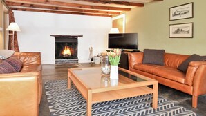Een woonkamer met een open haard, leren banken, een salontafel en een televisie.