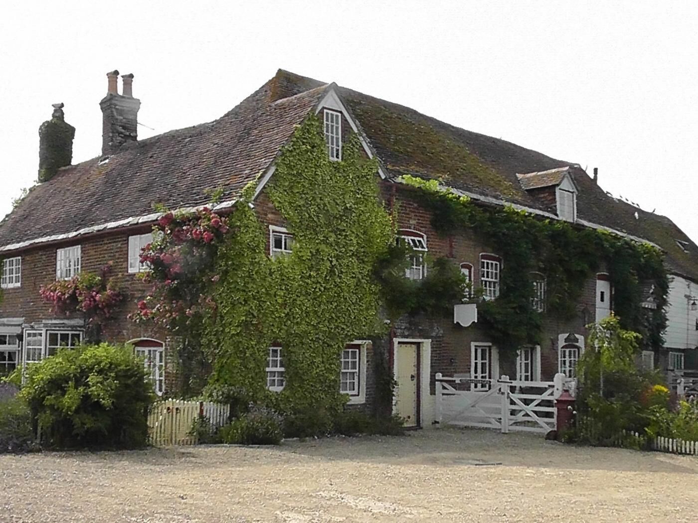 Un bâtiment traditionnel en briques, doté d’un toit à forte pente, de murs recouverts de lierre et d’une entrée fermée par un portail.