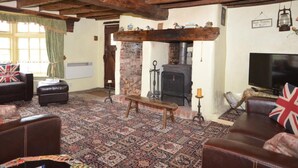 Ein traditionelles Wohnzimmer mit Kamin aus Stein, Holzbalken, einem Fernseher und einem gemusterten Teppich.