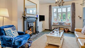 A living room with a fireplace, a television, a sofa, a coffee table, and a window with curtains. - 2 Bed in Wells (oc-wesba) (Wookey Hole)
