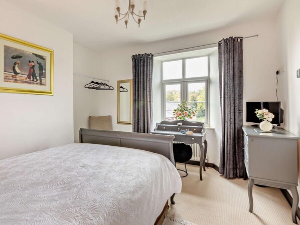 A bedroom with a bed, a desk, a chair, a TV, and a window with curtains.