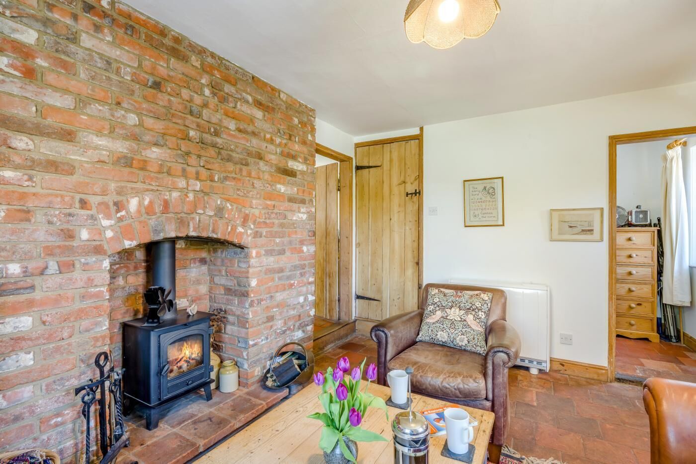 A cozy living room with a brick fireplace, a leather sofa, a wooden coffee table, and a radiator.