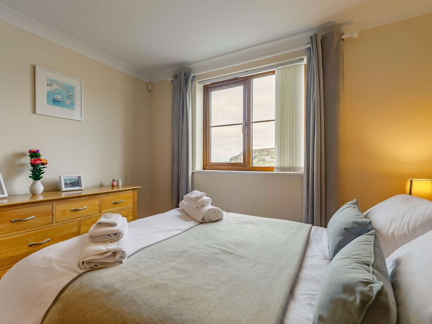 A hotel room with a bed, a dresser, a window with curtains, and a wall-mounted picture.