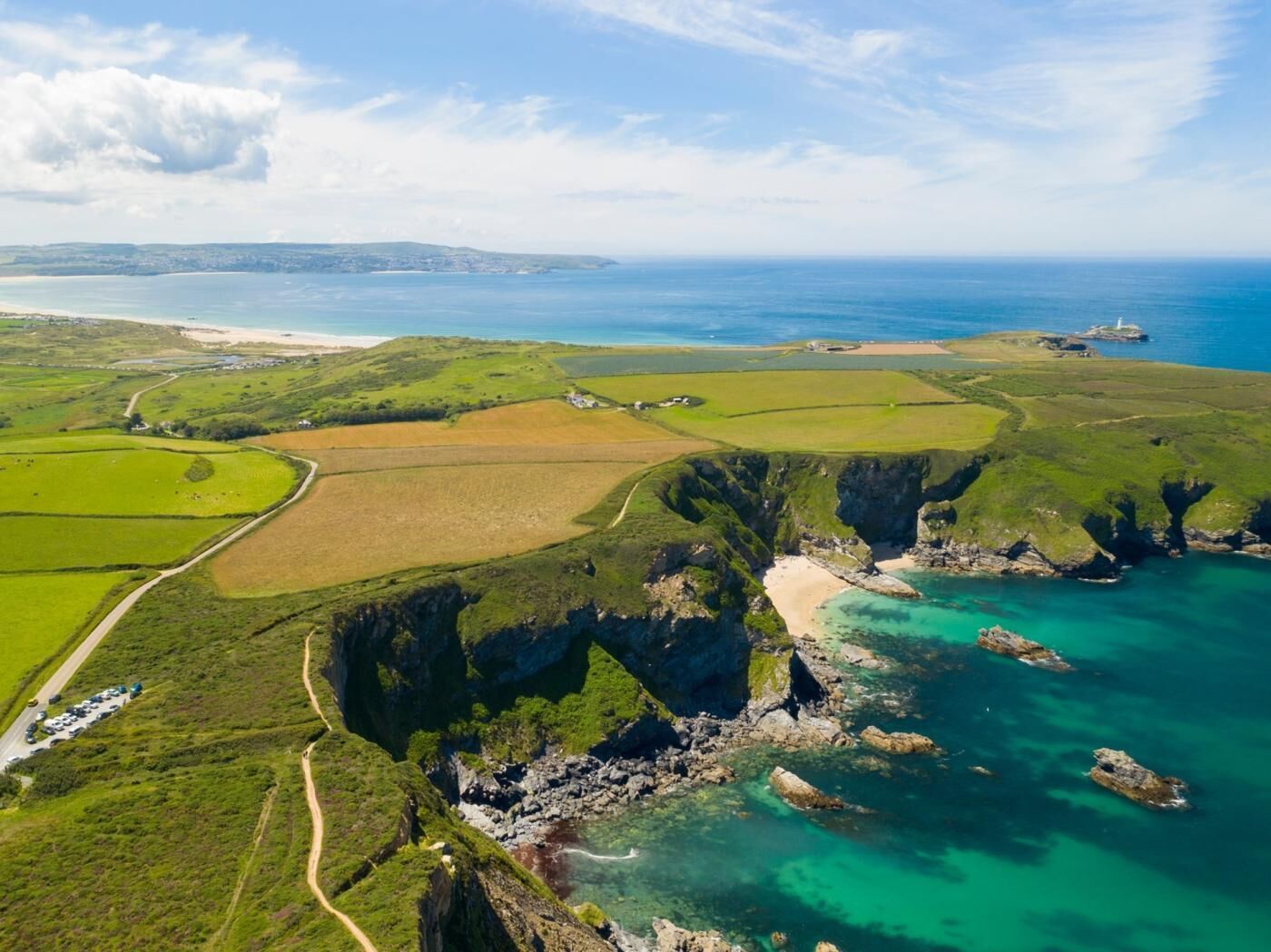 An aerial view of a coastal landscape with fields, cliffs, and a lighthouse.