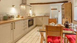 Una cocina con gabinetes blancos, encimera de madera, horno empotrado y comedor con mesa de vidrio y sillas de madera.
