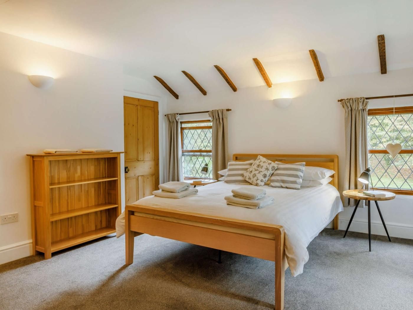 A bedroom with a wooden bed, a bedside table with a lamp, a wardrobe, and a window with curtains.