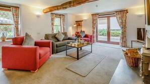 Una sala de estar amoblada con un sofá, un sillón y una mesa de centro. Hay una chimenea, una ventana con cortinas y una puerta que da al exterior.