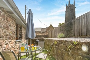 A stone building with a traditional design, a table with chairs, and a large umbrella. - 2 Bed in Bideford (oc-32240) (Fairy Cross)