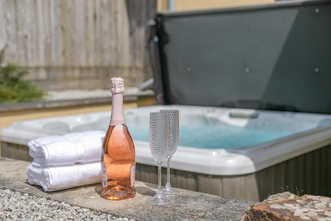 A hot tub with a bottle and a glass on a stone surface.
