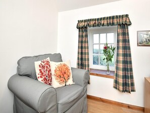 Ein graues Sofa mit zwei Zierkissen, ein Fenster mit Karottenstreifen-Vorhängen und eine Vase mit einer einzelnen roten Rose auf der Fensterbank.