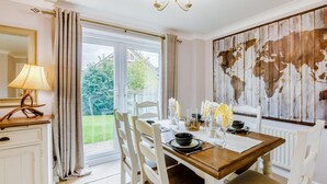 A dining area with a table set for four, a chandelier, a world map wall, and a view through a glass door. - 3 Bed in Alnwick (oc-36401) (Alnwick)