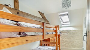 Ein Schlafraum mit Etagenbetten, einem Dachfenster, einem kleinen Fenster und einer dekorativen Leuchte.