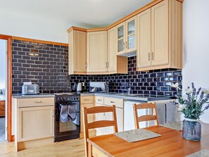 A kitchen with wooden cabinets, a black tiled backsplash, and a wooden dining table with chairs. - 2 Bed in Bristol (oc-37147) (Chew Magna)