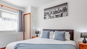 Ein Hotelzimmer mit Bett, einem Stadtbild, einem Vorhangfenster und einem Nachttisch mit Lampe.