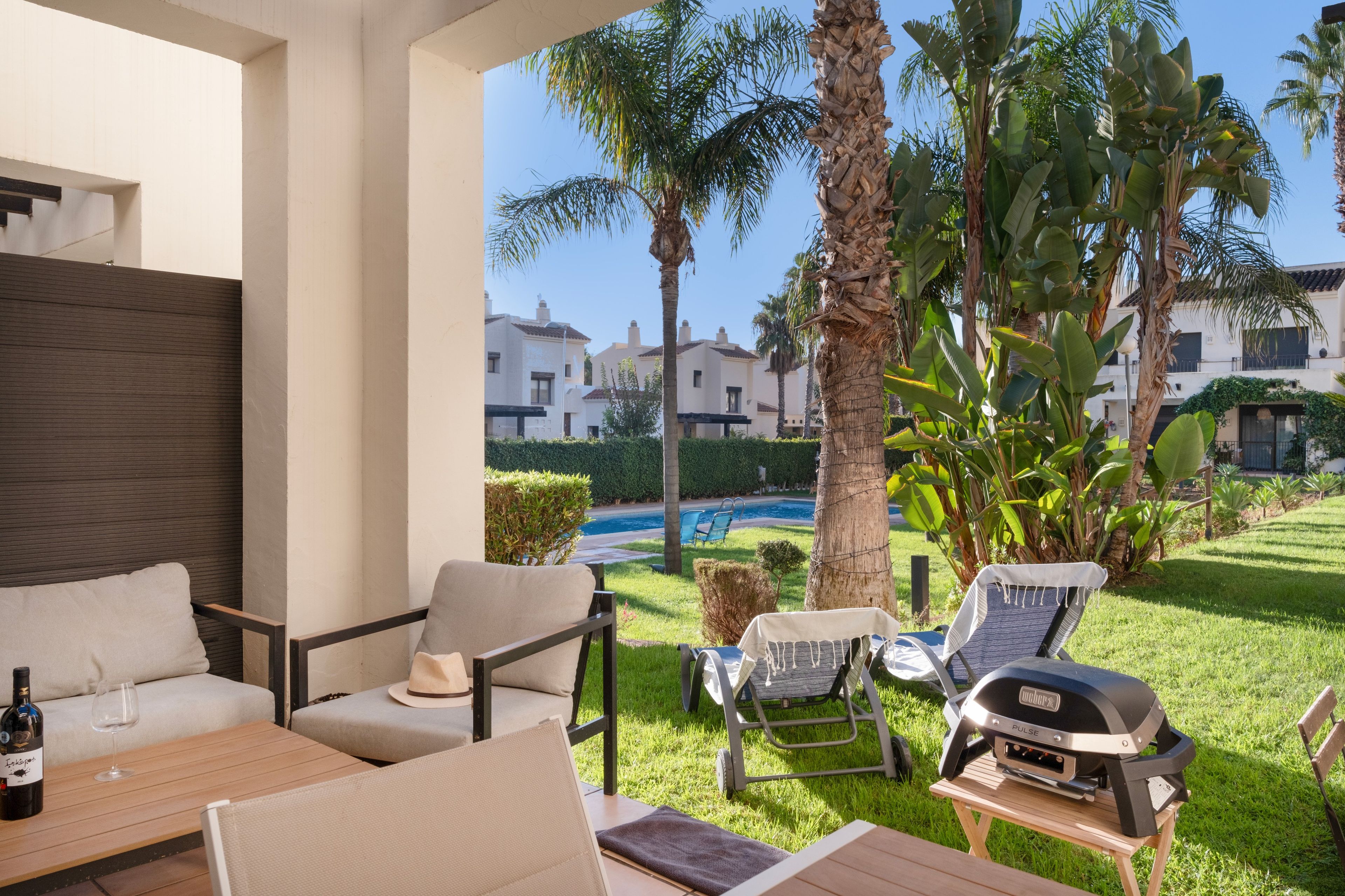 An outdoor seating area with a pool view, lounge chairs, and a barbecue grill.