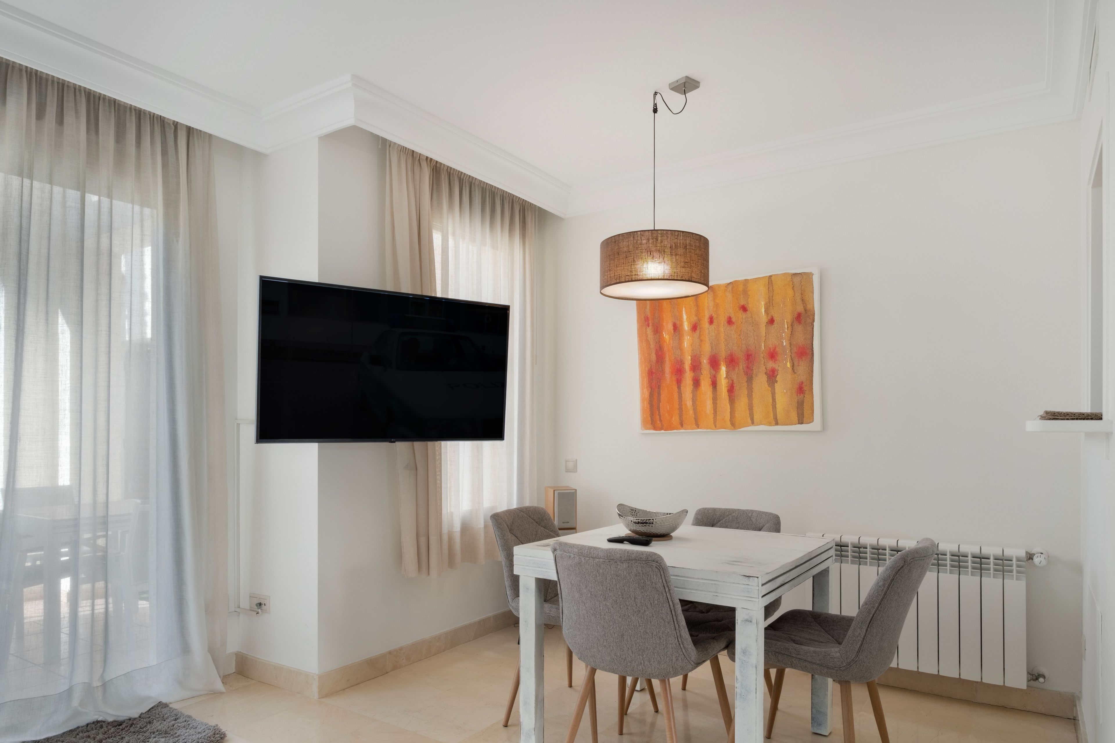 Un comedor moderno con un televisor de pantalla plana, una mesa con sillas, una lámpara colgante y un cuadro en la pared.