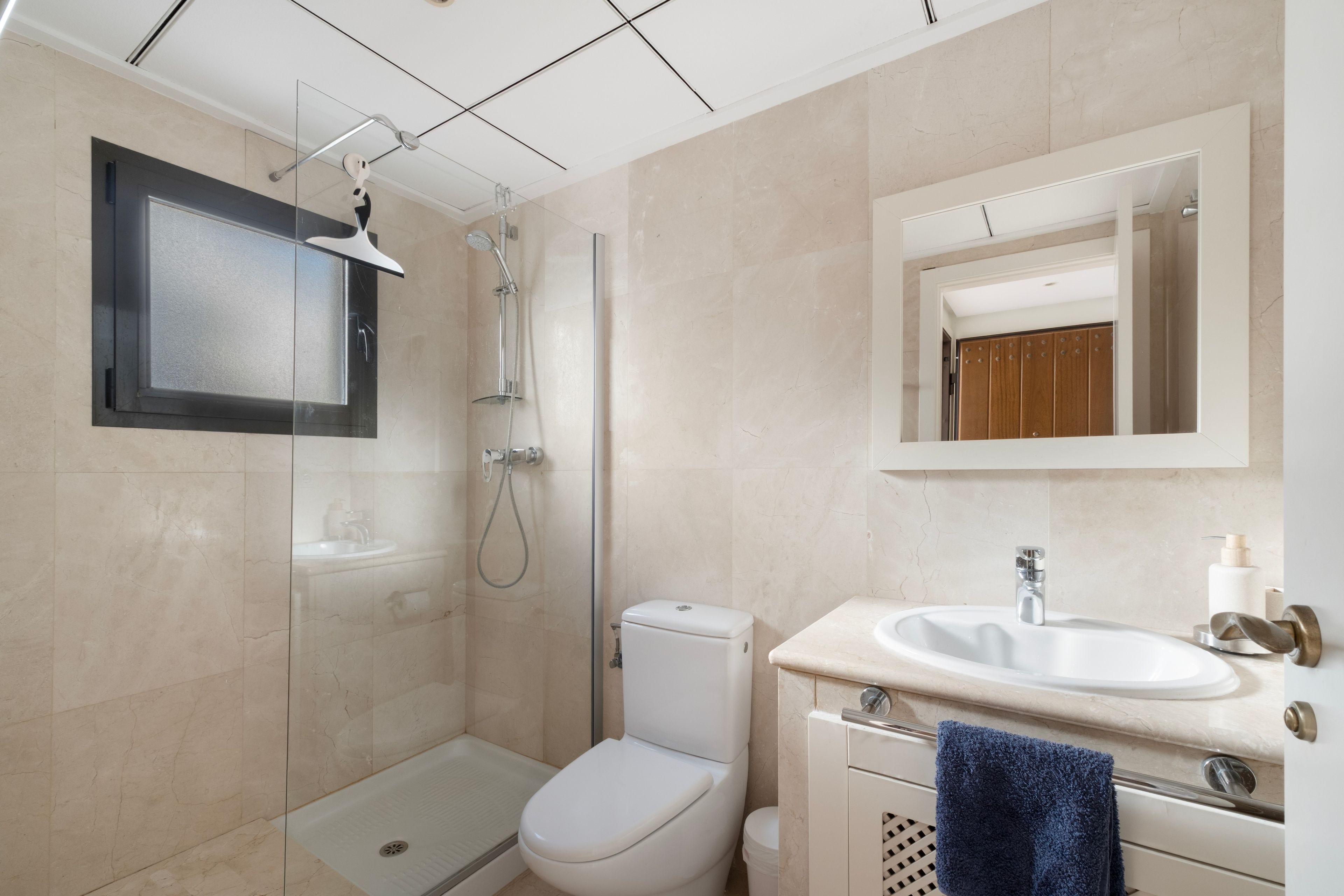 Un baño moderno con ducha envuelta en vidrio, inodoro y lavamanos con una toalla colgada a un lado.