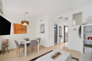A modern living room with a dining area, a kitchen visible through an open door, and a television mounted on the wall. - Holiday Home 'Casa Thomas II Terraced Corner' with Shared Pool, Wi-Fi and Air Conditioning (Roda)