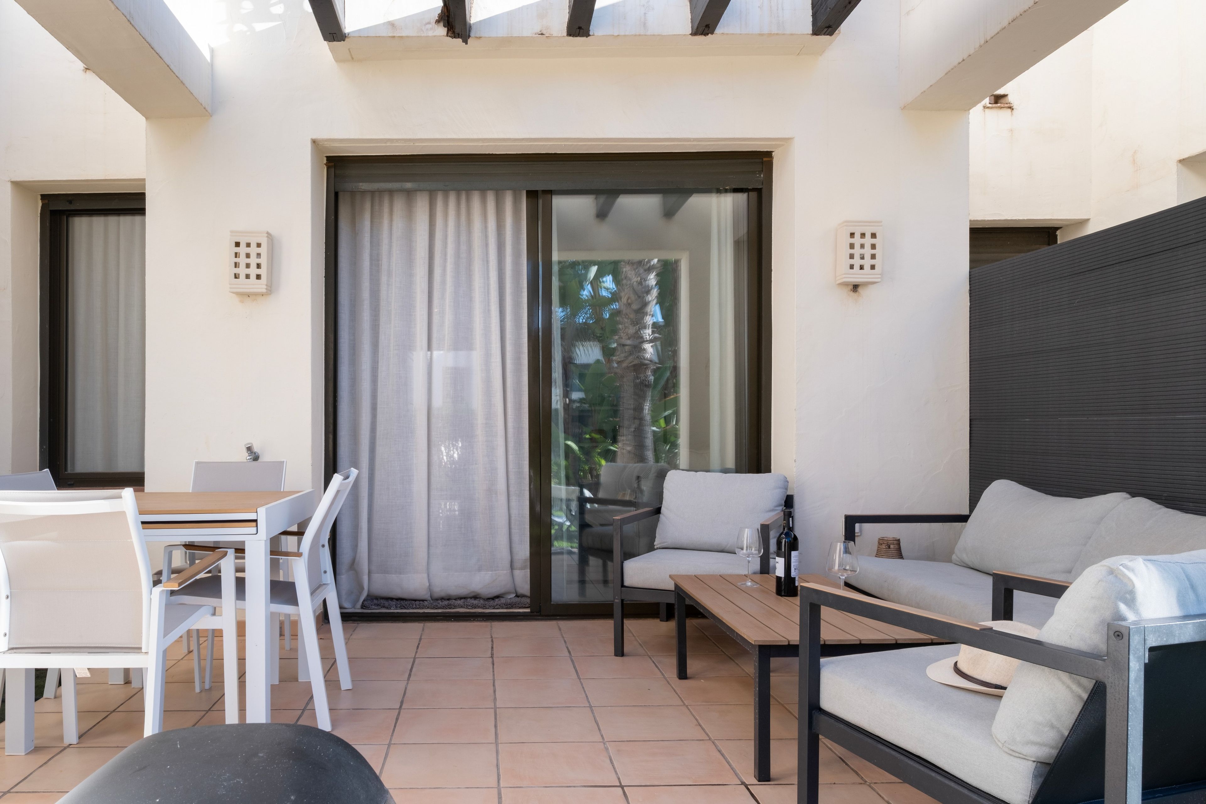 Un patio soleado con una mesa de comedor, sillas, un sofá y un banco.