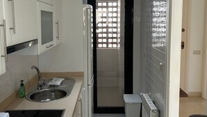 Cocina compacta con un lavamanos, un refrigerador y una ventana con diseño de cuadrícula.