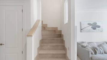 Una escalera con peldaños color beige que lleva a un rellano, una puerta blanca a la izquierda y un sofá gris con cojines estampados a la derecha.