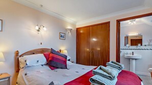 Ein Hotelzimmer mit Bett, Nachttischen, einem Kleiderschrank und einem Badezimmer mit Waschbecken und Spiegel.