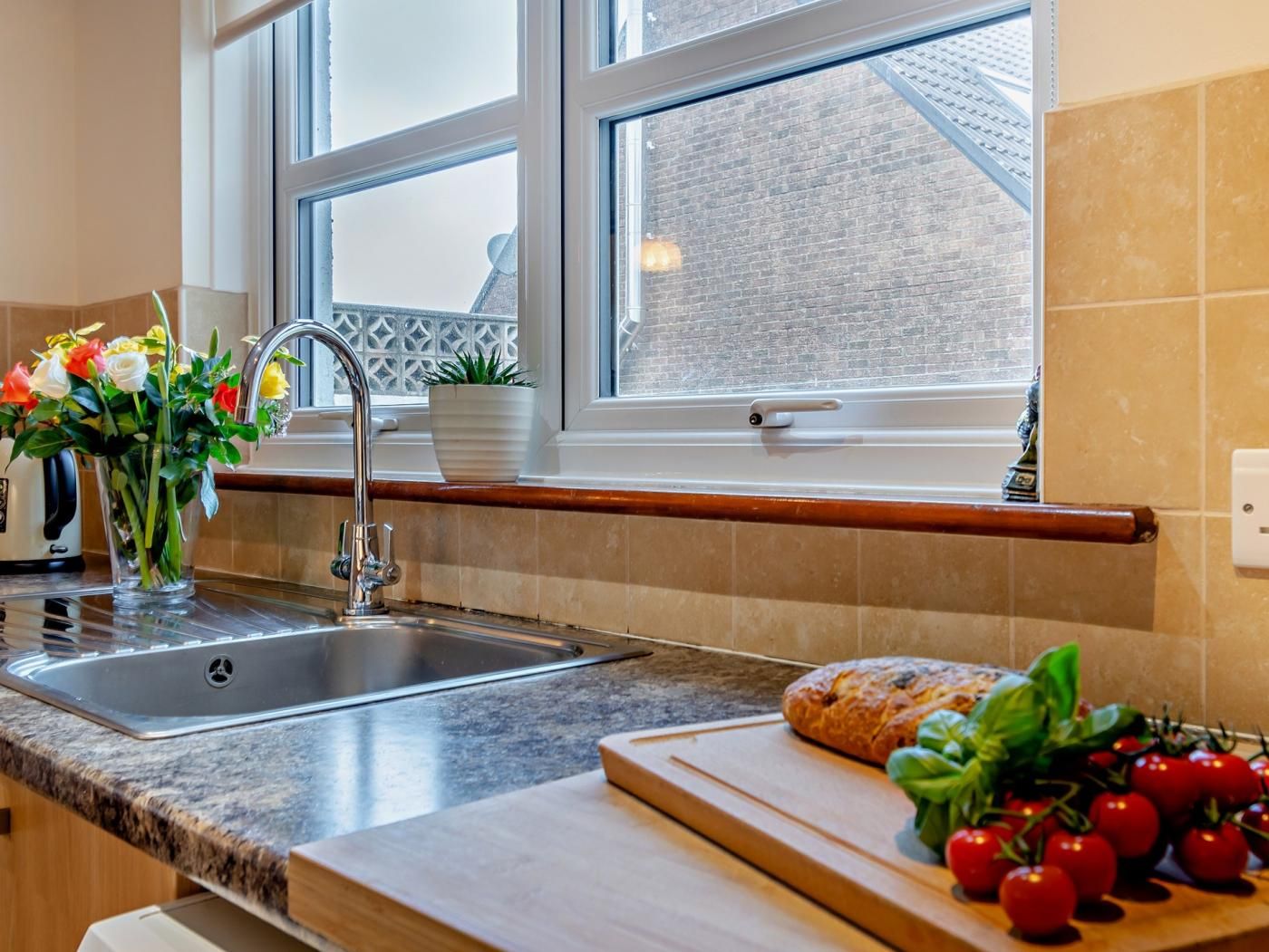 A kitchen with a granite countertop, stainless steel sink, and a window with a view of a brick building.