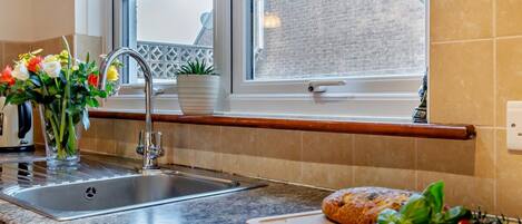 Una cocina con encimera de granito, pileta de acero inoxidable y ventana con vista a un edificio de ladrillo.