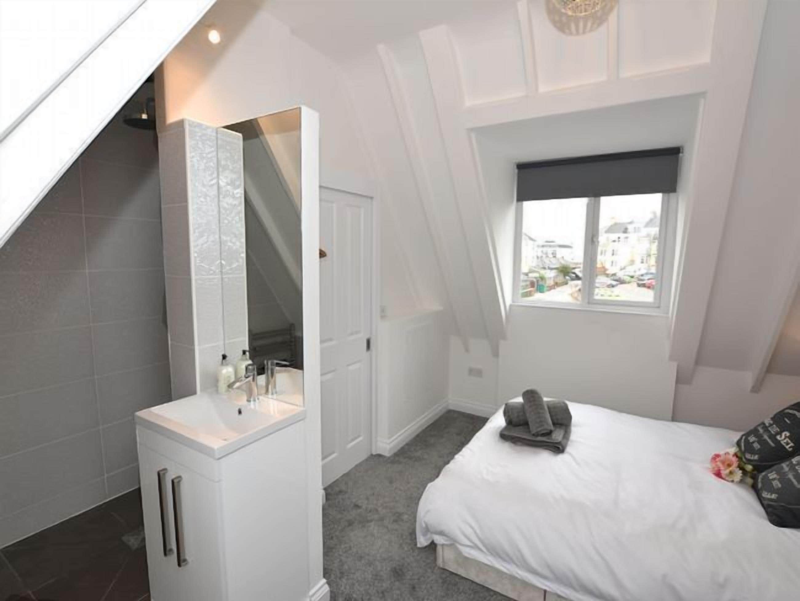 Un dormitorio con tragaluz, cama, mesita de noche, espejo y ventana.