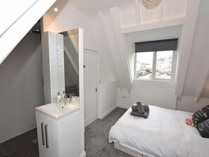 Ein Schlafzimmer mit Dachfenster, einem Bett, einem Nachttisch, einem Spiegel und einem Fenster.