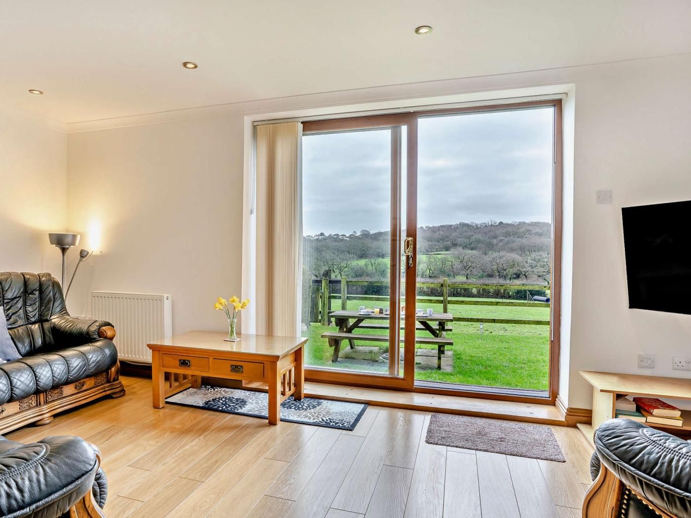 Sala de estar com sofá, mesa de centro e vista para uma paisagem verde através de uma porta de correr de vidro.